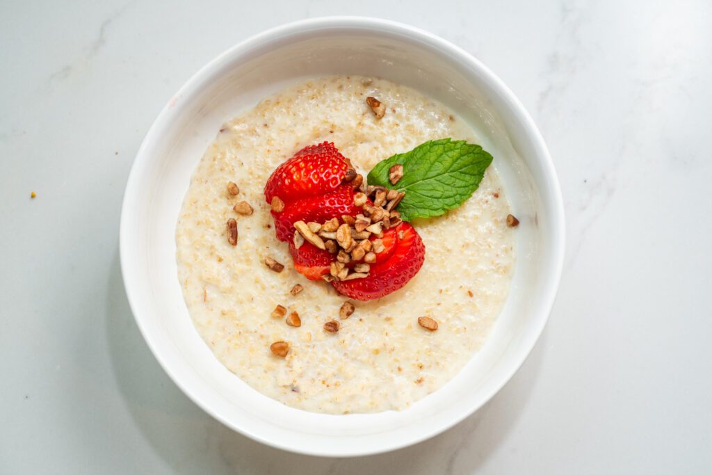 A bowl of oatmeal topped with strawberries, granola, and a mint leaf on a marble surface.