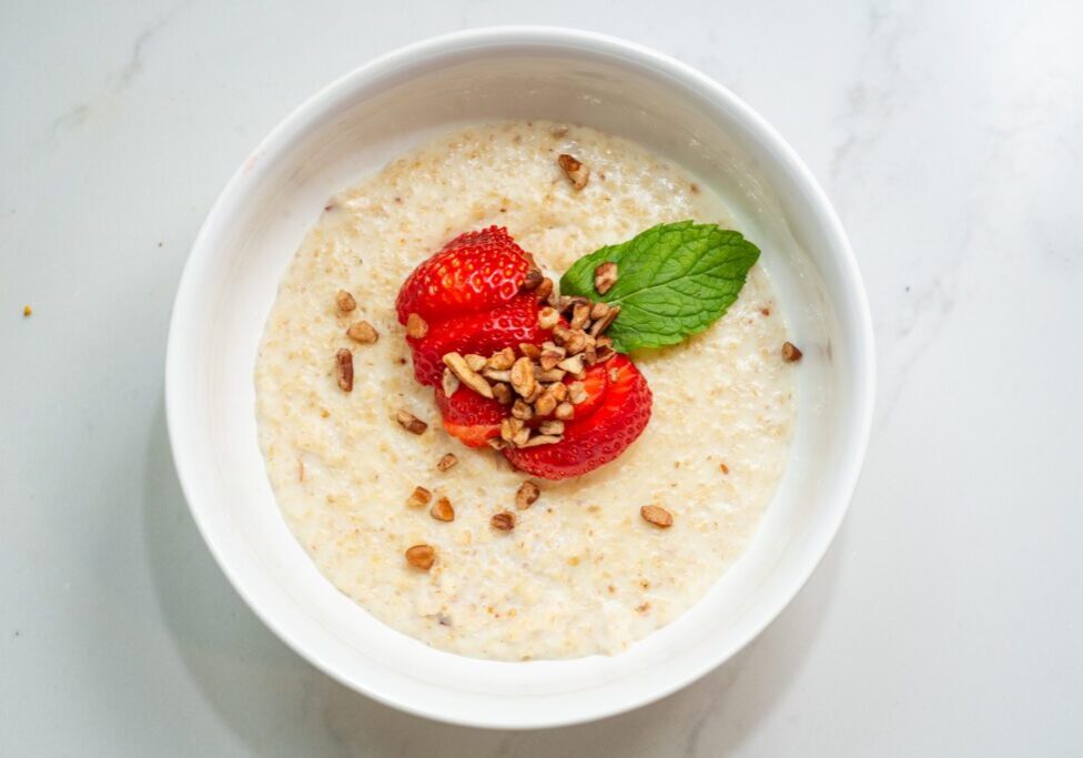 A bowl of oatmeal topped with strawberries, granola, and a mint leaf on a marble surface.